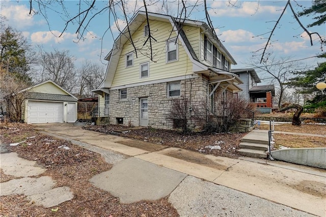 view of property exterior featuring driveway, stone siding, a detached garage, and an outbuilding