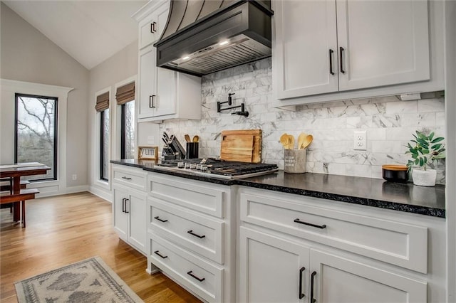 kitchen with decorative backsplash, stainless steel gas cooktop, lofted ceiling, custom exhaust hood, and white cabinets