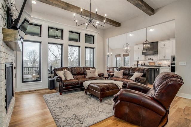 living area with beam ceiling, a fireplace, recessed lighting, light wood finished floors, and a notable chandelier