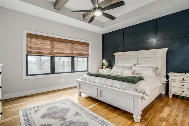 bedroom with ceiling fan, visible vents, wood finished floors, baseboards, and a tray ceiling
