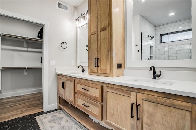 bathroom with visible vents, a sink, a tile shower, and double vanity