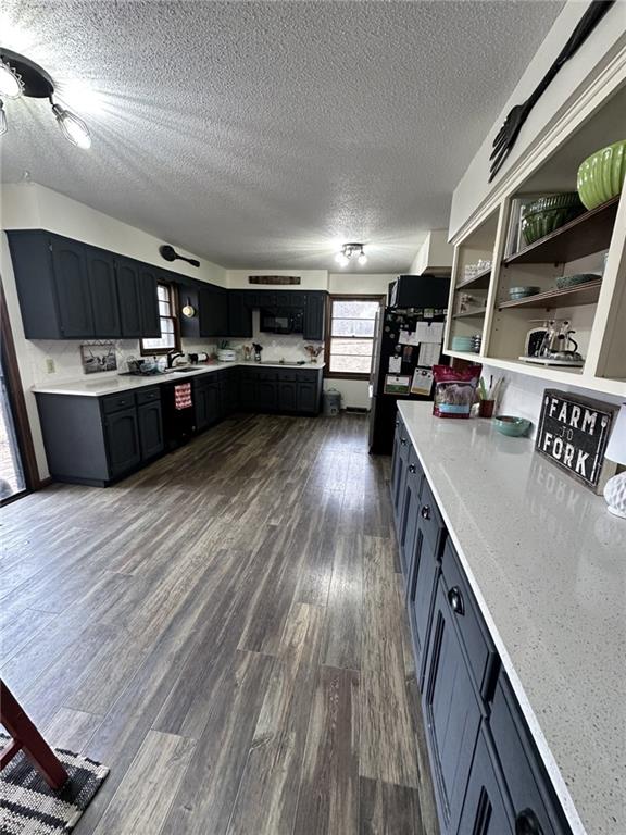 kitchen with a textured ceiling, a sink, light countertops, open shelves, and dark wood finished floors