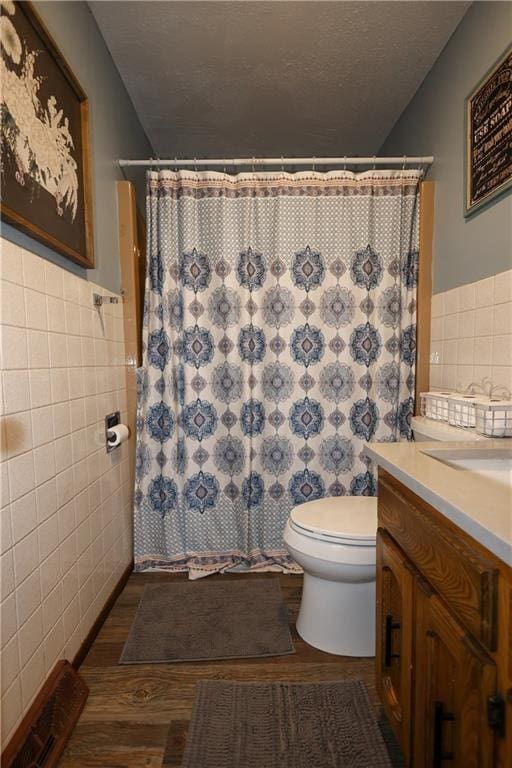 full bath with toilet, a shower with curtain, a textured ceiling, vanity, and tile walls