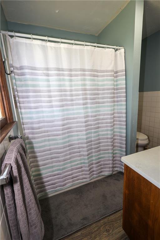 full bath featuring tile walls, curtained shower, toilet, wainscoting, and vanity