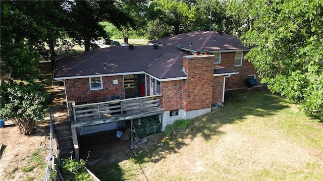 rear view of house with a chimney, brick siding, a lawn, and a deck