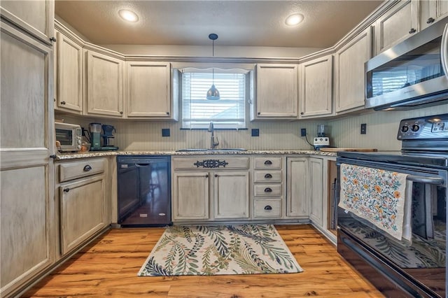 kitchen featuring decorative light fixtures, light wood-type flooring, light stone counters, black appliances, and a sink