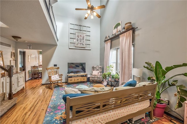 living room featuring stairway, a ceiling fan, wood finished floors, a towering ceiling, and a textured ceiling