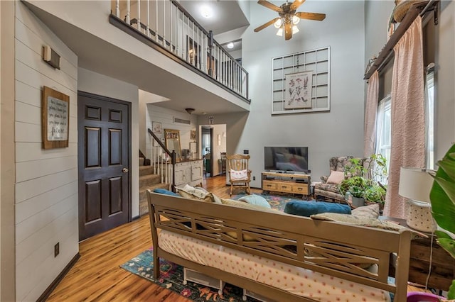 living area with wooden walls, wood finished floors, a high ceiling, ceiling fan, and stairs