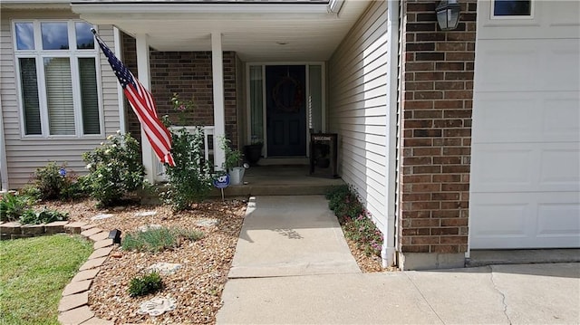 doorway to property featuring brick siding, covered porch, and a garage