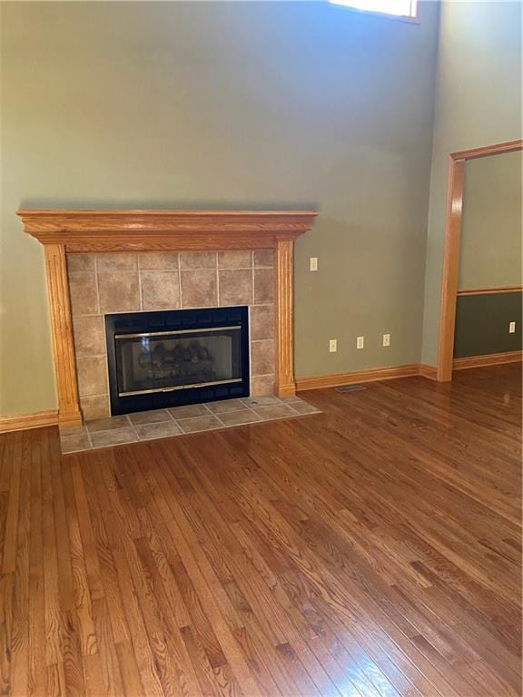 unfurnished living room with a tiled fireplace, baseboards, and wood finished floors