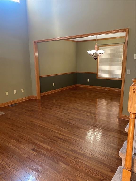 spare room featuring visible vents, a notable chandelier, wood finished floors, and baseboards