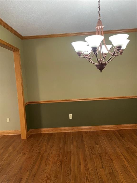 empty room featuring an inviting chandelier, wood finished floors, baseboards, and ornamental molding