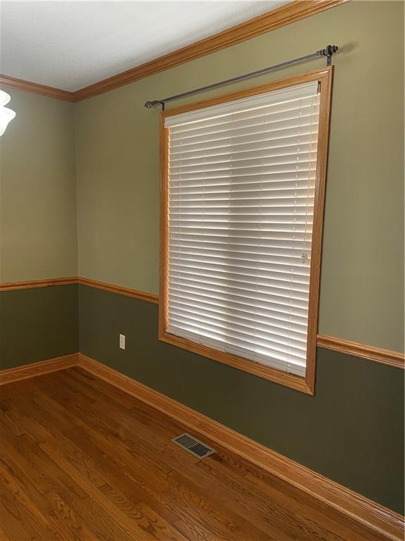 spare room featuring crown molding, wood finished floors, visible vents, and baseboards