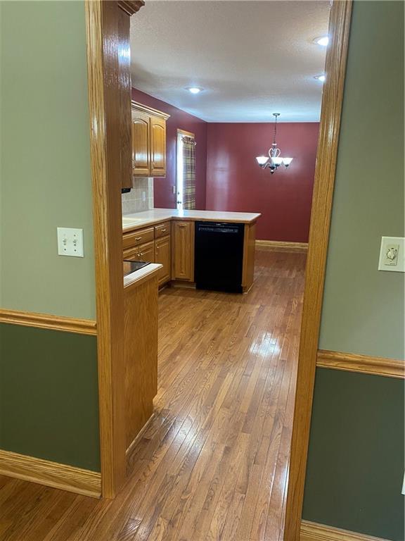 kitchen with baseboards, a peninsula, light countertops, black dishwasher, and light wood-type flooring