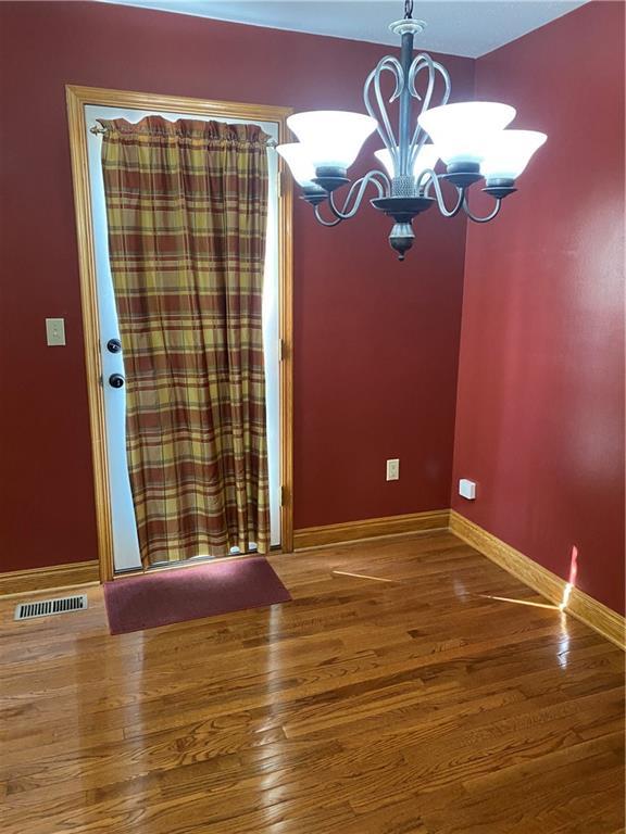 unfurnished dining area with a notable chandelier, visible vents, baseboards, and wood finished floors