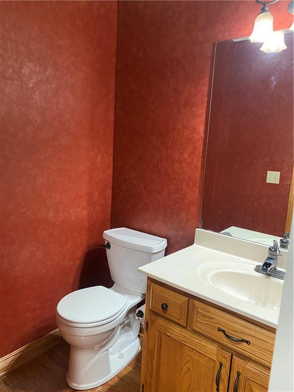 half bathroom featuring baseboards, toilet, wood finished floors, and vanity