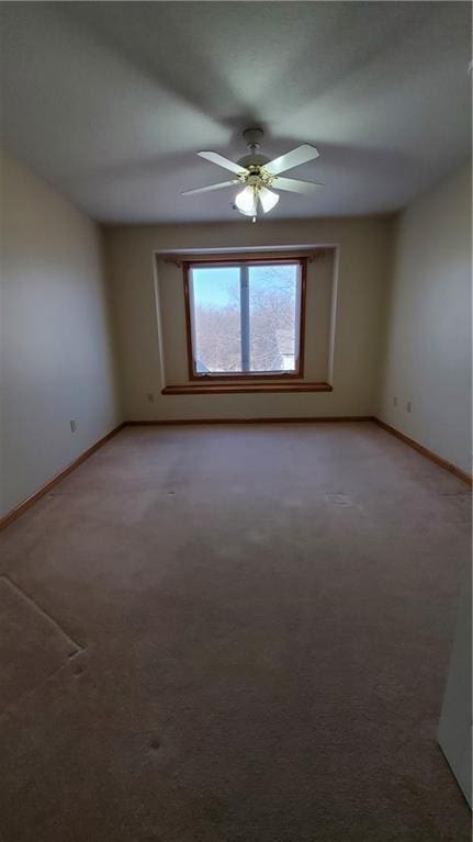 empty room featuring a ceiling fan, light colored carpet, and baseboards