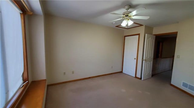 carpeted spare room featuring baseboards, visible vents, and ceiling fan