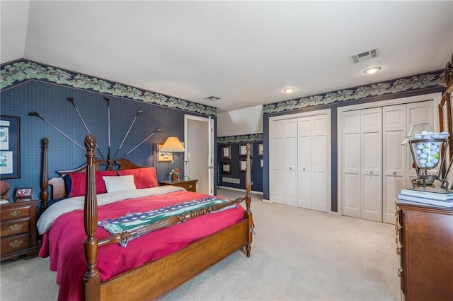 carpeted bedroom with wallpapered walls, vaulted ceiling, visible vents, and multiple closets