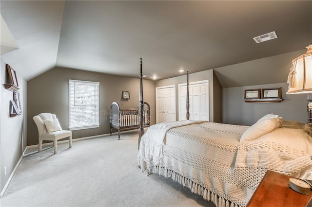 bedroom with visible vents, multiple closets, lofted ceiling, baseboards, and light colored carpet