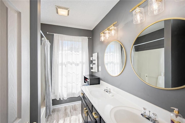 bathroom with double vanity, visible vents, a textured ceiling, and a sink