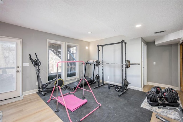 exercise area with wood finished floors, visible vents, baseboards, and a textured ceiling