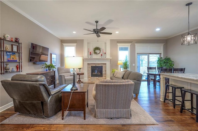 living room with dark wood finished floors, recessed lighting, ornamental molding, a stone fireplace, and baseboards