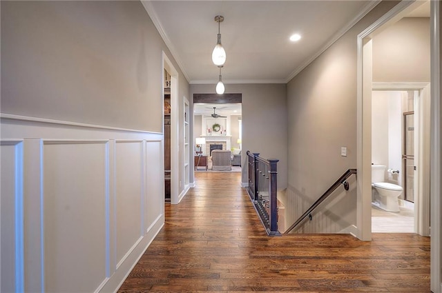 hall featuring wainscoting, dark wood-style floors, ornamental molding, an upstairs landing, and a decorative wall