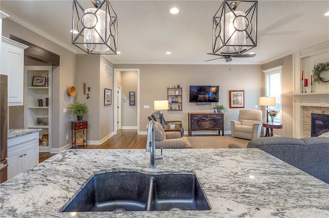 interior space with crown molding, light stone countertops, a glass covered fireplace, a sink, and wood finished floors