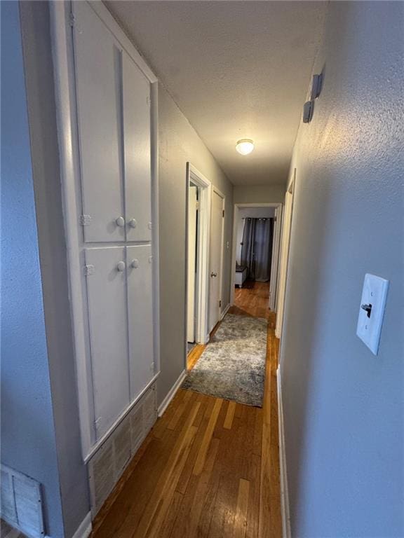 hallway with baseboards, visible vents, and dark wood finished floors