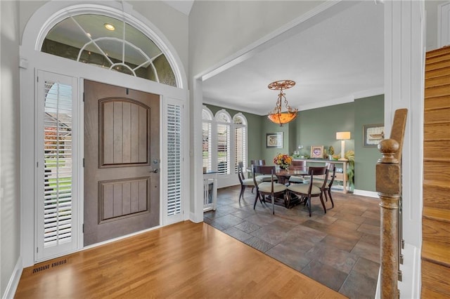 foyer entrance with ornamental molding, wood finished floors, visible vents, and baseboards