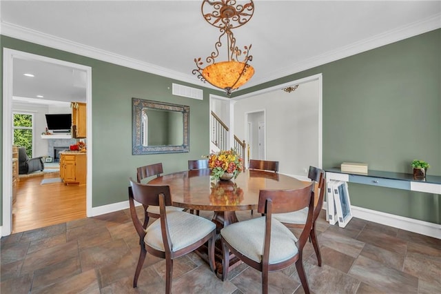 dining room with a fireplace, visible vents, ornamental molding, baseboards, and stairs