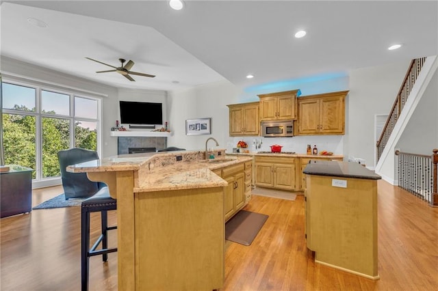 kitchen featuring stainless steel microwave, a sink, an island with sink, light stone countertops, and a kitchen bar