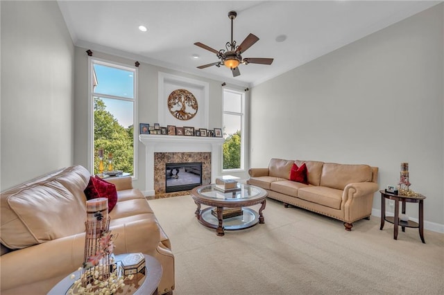 living room with carpet, ornamental molding, a high end fireplace, ceiling fan, and baseboards