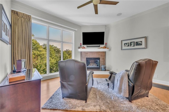 sitting room featuring crown molding, a tiled fireplace, ceiling fan, wood finished floors, and baseboards