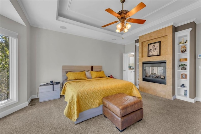 carpeted bedroom featuring a tile fireplace, a ceiling fan, baseboards, ornamental molding, and a raised ceiling