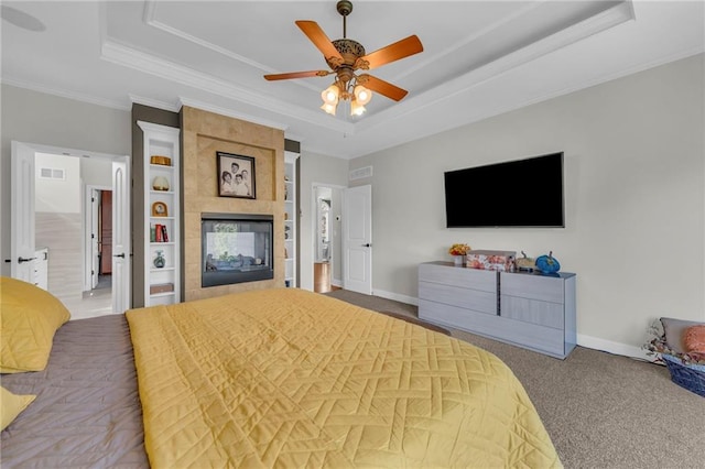 bedroom with carpet floors, a tiled fireplace, a raised ceiling, and baseboards