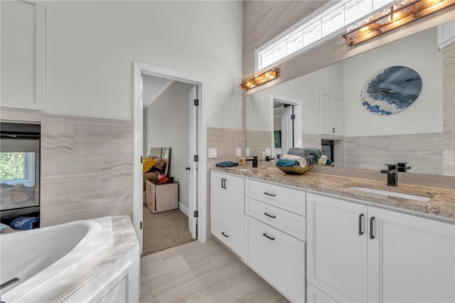 full bathroom featuring a bathtub, a sink, tile walls, and double vanity