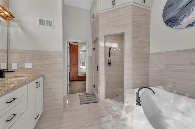 bathroom with a stall shower, visible vents, a jetted tub, vanity, and tile walls