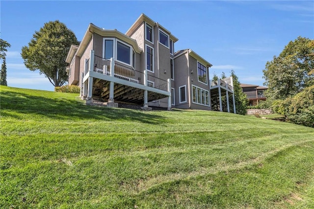 rear view of house with stairs, a yard, a deck, and stucco siding