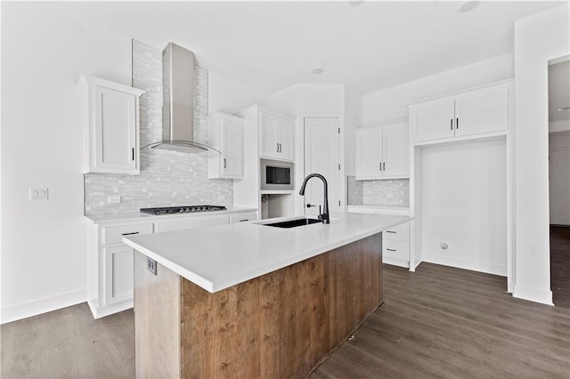 kitchen with white cabinets, stainless steel microwave, wall chimney range hood, gas stovetop, and a sink