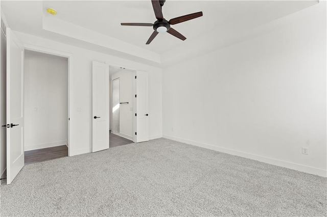 unfurnished bedroom with a tray ceiling, carpet, a ceiling fan, and baseboards