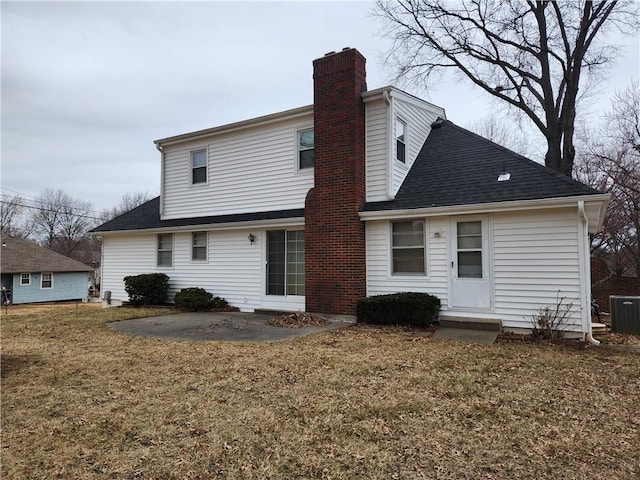 rear view of property featuring a lawn, central AC unit, roof with shingles, and a patio area