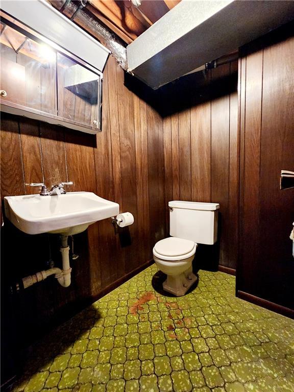 half bathroom with tile patterned floors, wooden walls, a sink, and toilet