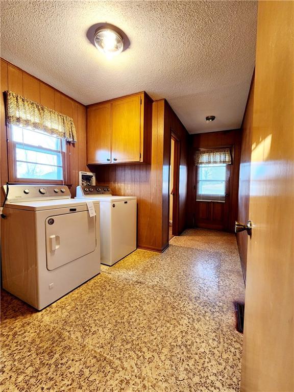 laundry area with cabinet space, a textured ceiling, wood walls, and separate washer and dryer