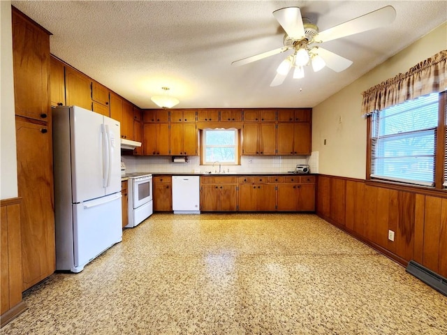 kitchen featuring a wainscoted wall, a textured ceiling, white appliances, wood walls, and brown cabinetry