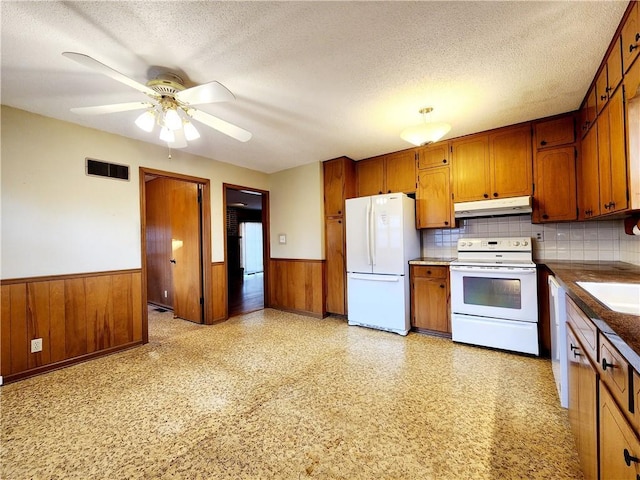 kitchen with visible vents, under cabinet range hood, wainscoting, white appliances, and a textured ceiling