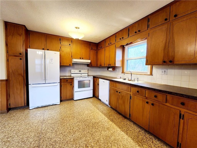 kitchen with white appliances, brown cabinetry, light floors, a sink, and under cabinet range hood