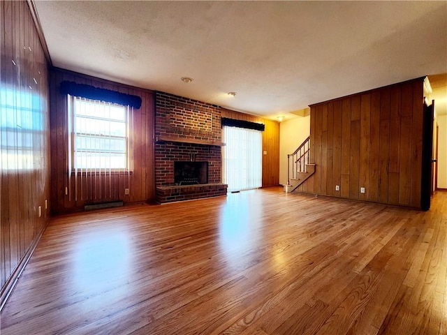 unfurnished living room with light wood-style floors, a brick fireplace, wood walls, and stairs