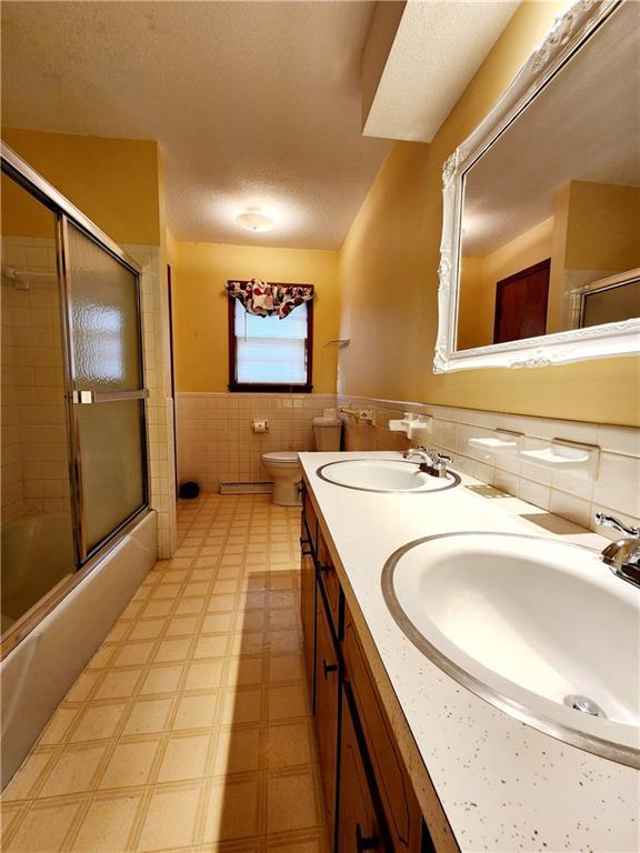 full bathroom featuring a sink, a wainscoted wall, a textured ceiling, and tile walls